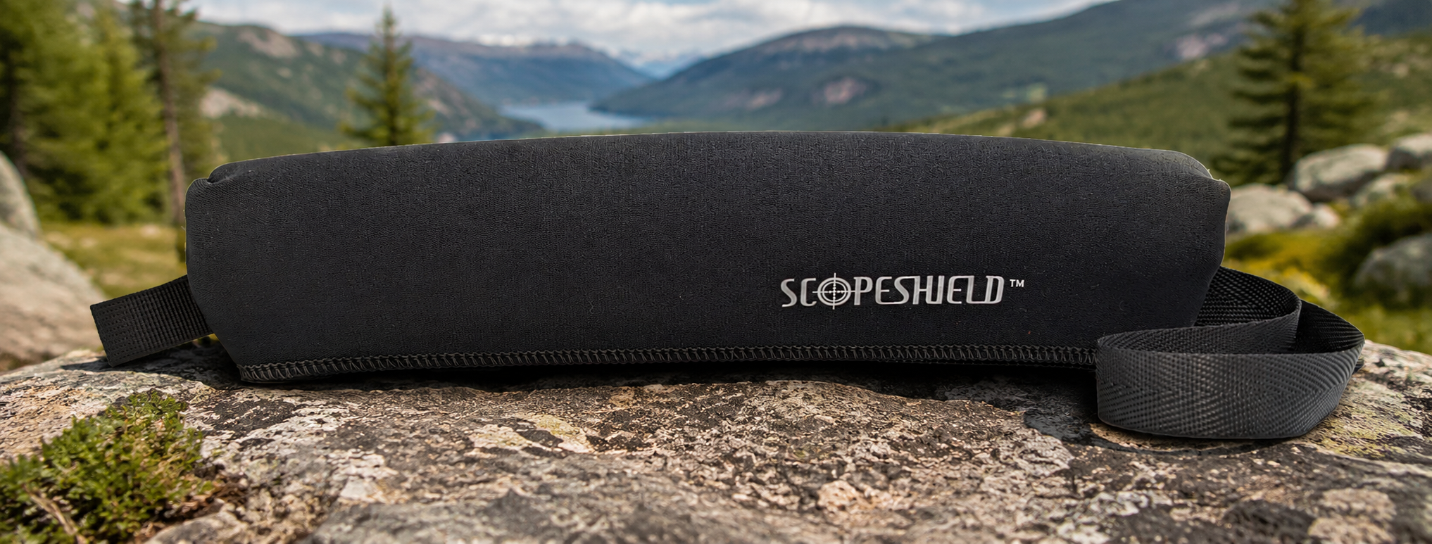 Black ScopeShield neoprene rifle scope cover displayed outdoors in a mountain setting