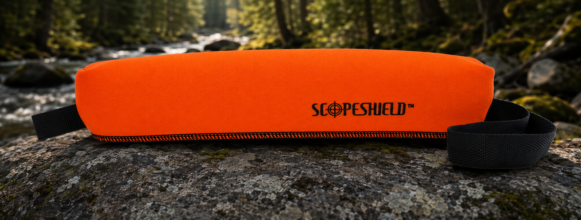 Hunter orange ScopeShield neoprene rifle scope cover displayed outdoors beside a forest stream