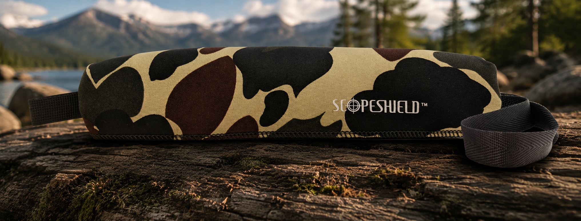 Camouflage ScopeShield neoprene rifle scope cover displayed outdoors near a mountain lake